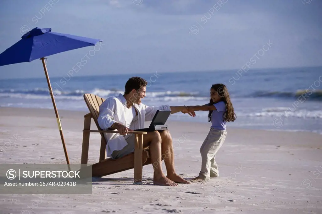 Father working on a laptop with his daughter pulling at his arm