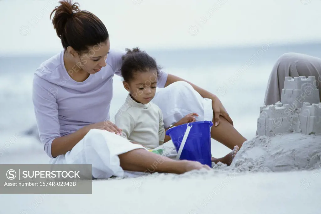 Woman sitting on a beach with her daughter building a sandcastle