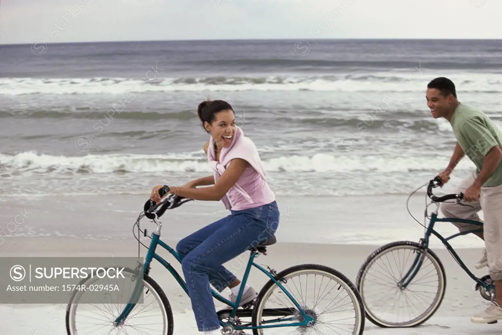 Side profile of a young couple cycling on the beach