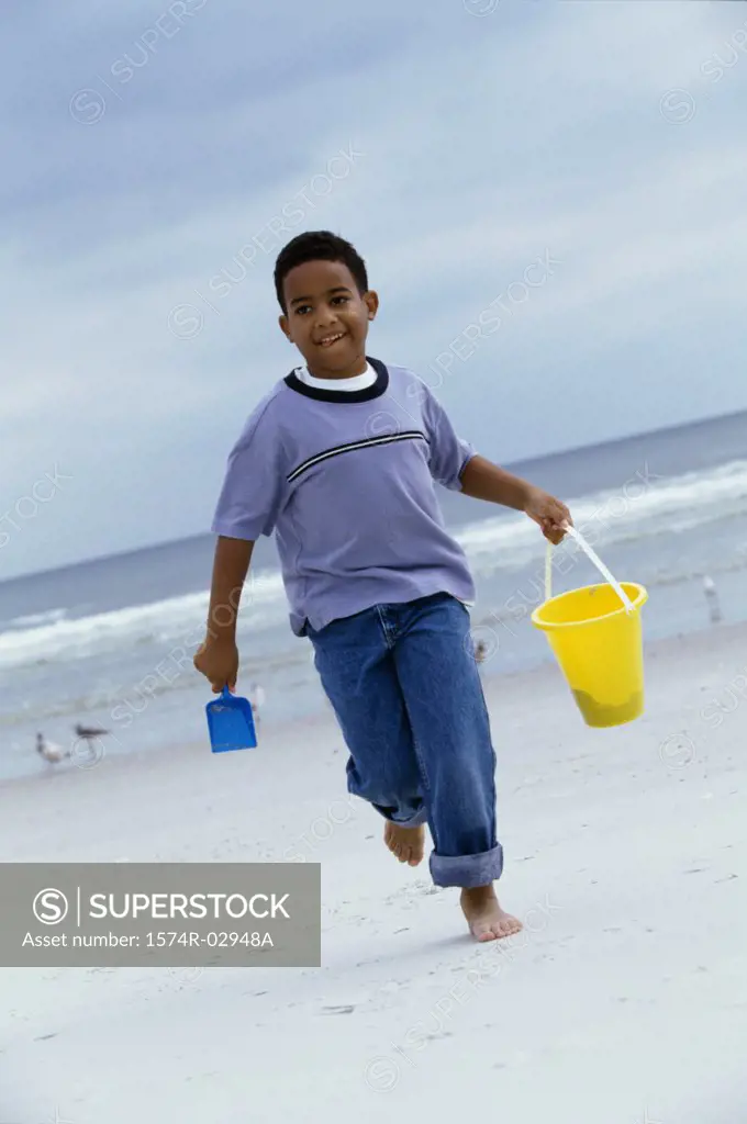Boy running on the beach carrying a sand pail