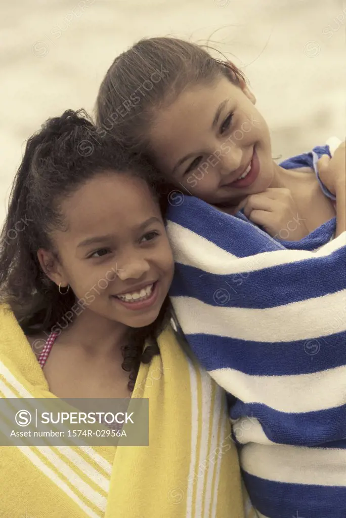 Two girls wrapped in towels on the beach