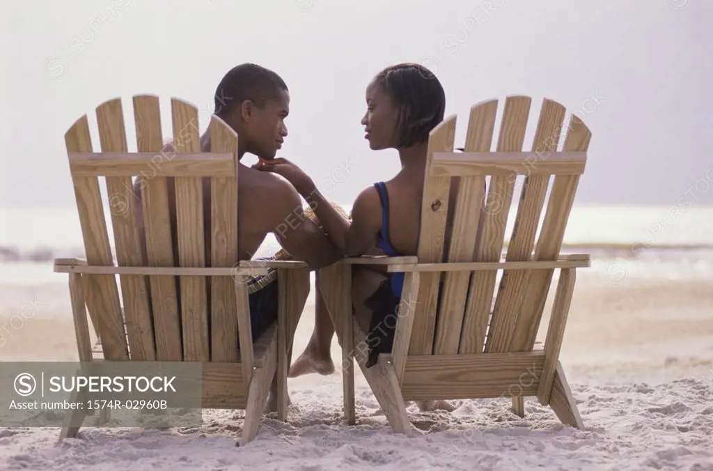 Rear view of a young couple sitting in chairs on the beach