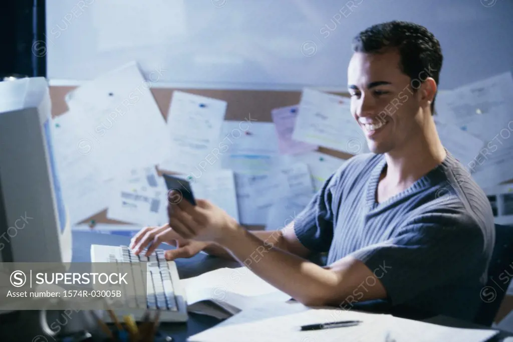 Side profile of a young man working on a computer holding a credit card