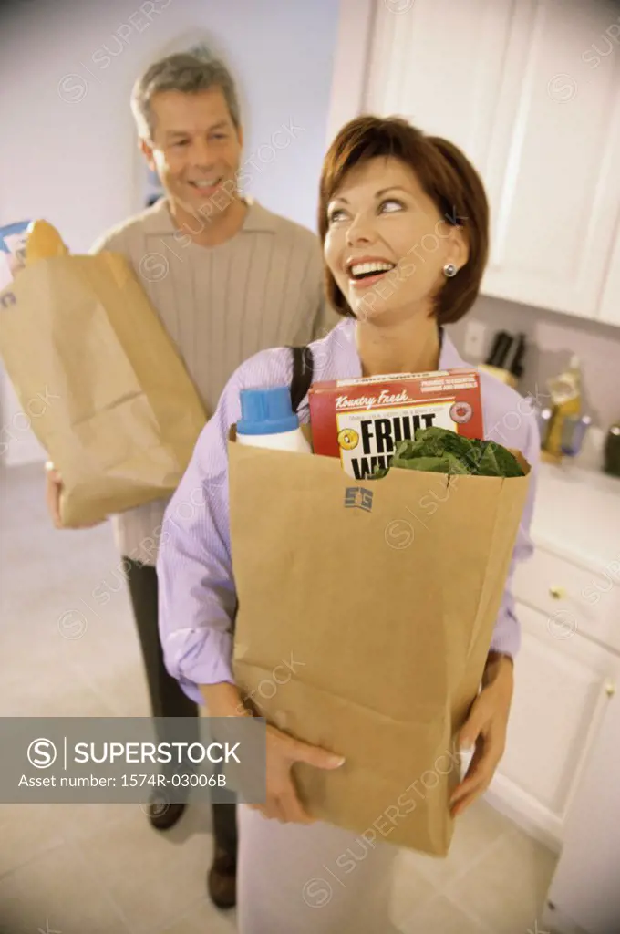 Mid adult couple standing in a kitchen holding grocery bags