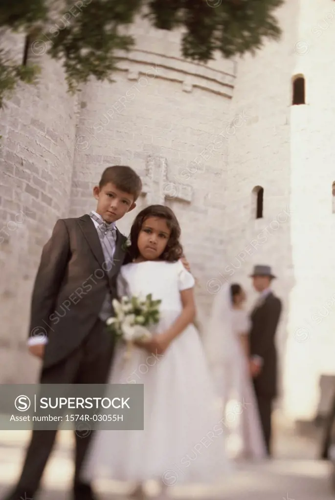 Portrait of a ring bearer and a flower girl standing in front of a church