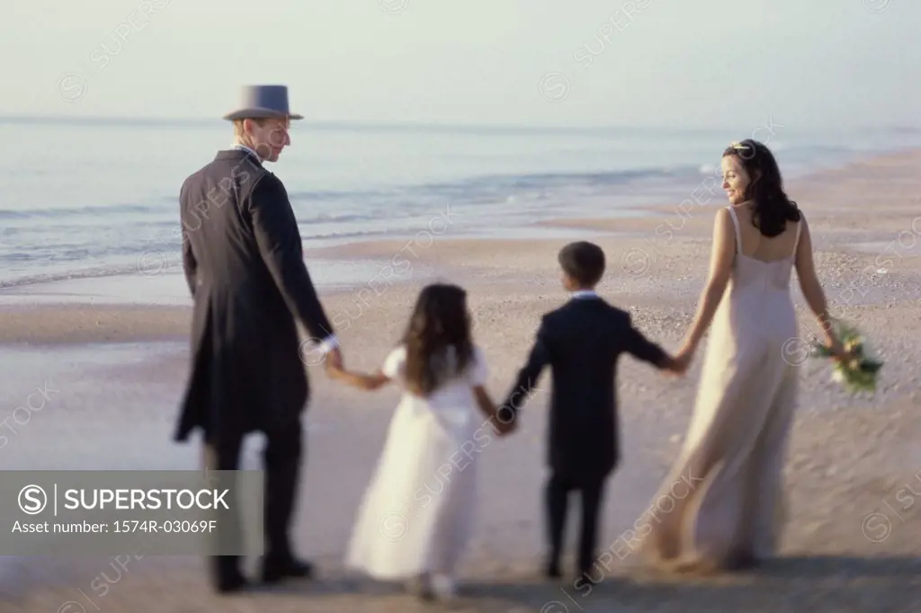 Rear view of a newlywed couple walking on the beach with a flower girl and a ring bearer
