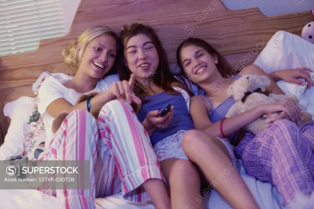 Three teenage girls lying on a bed watching television