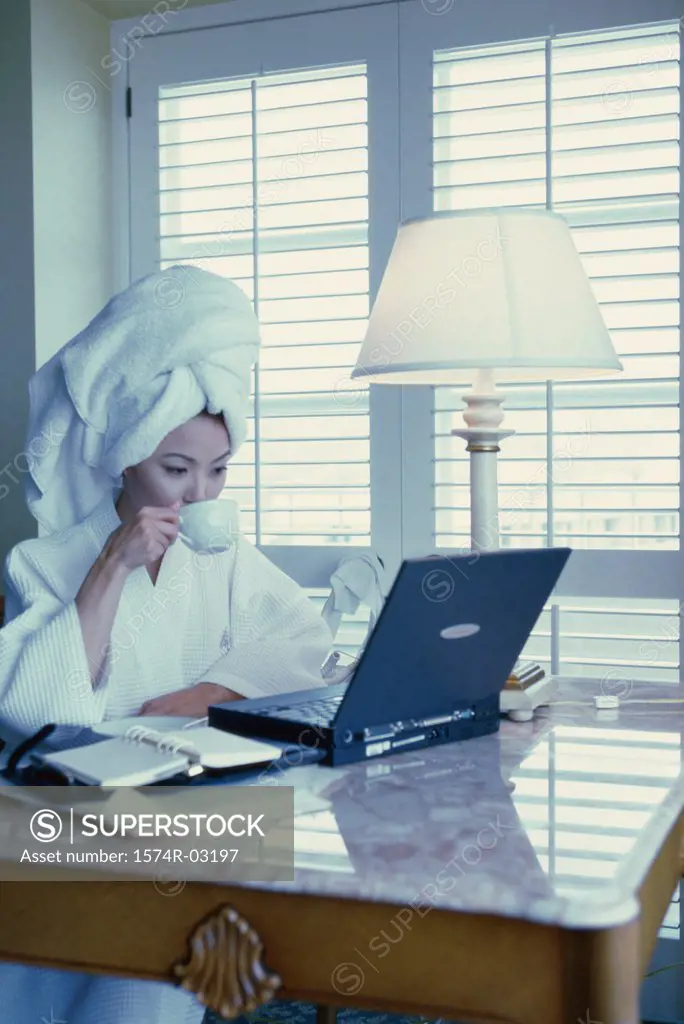 Young woman wearing a bathrobe sitting in front of a laptop in a hotel room