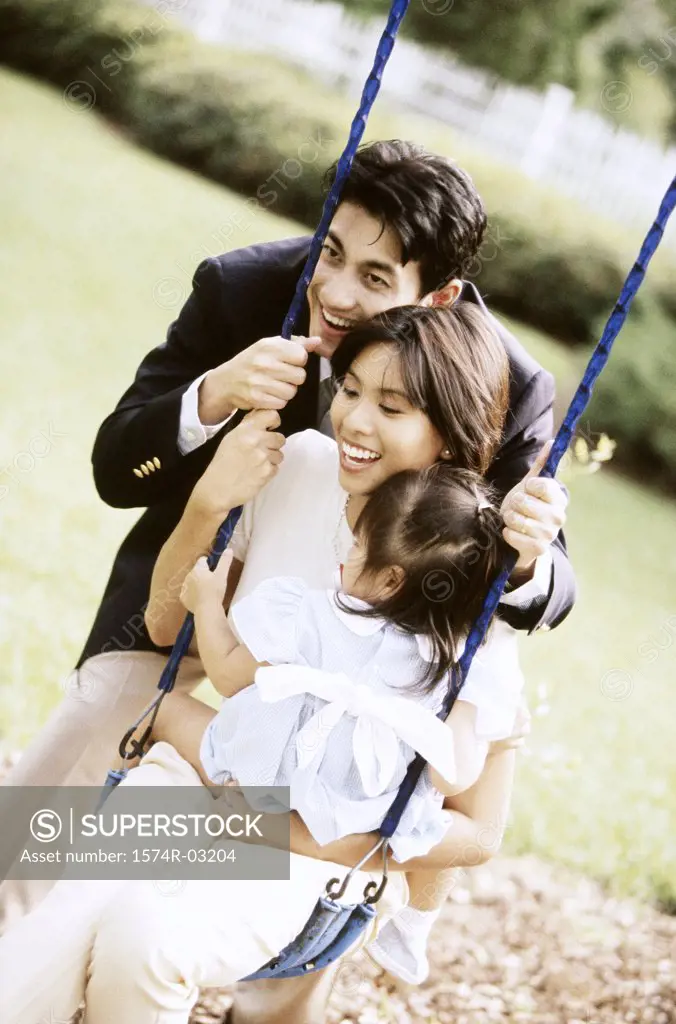Close-up of parents playing with their daughter on a swing