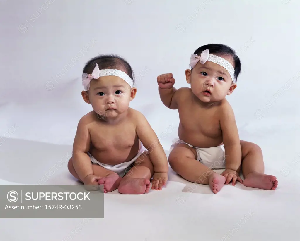 Portrait of two baby girls wearing diapers and bows on their heads