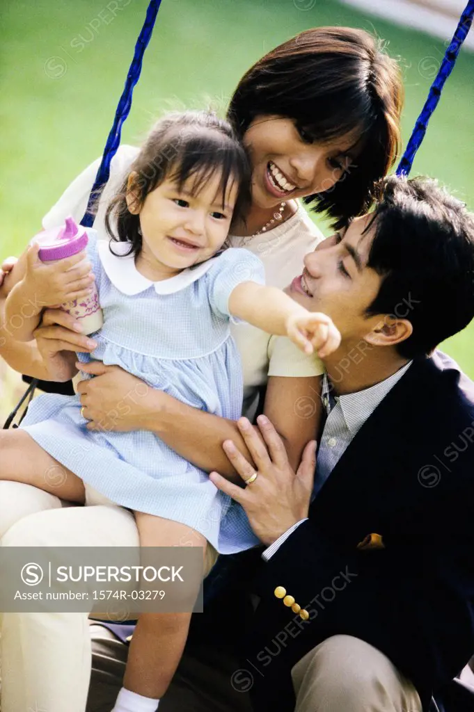 Close-up of parents playing with their daughter on a swing