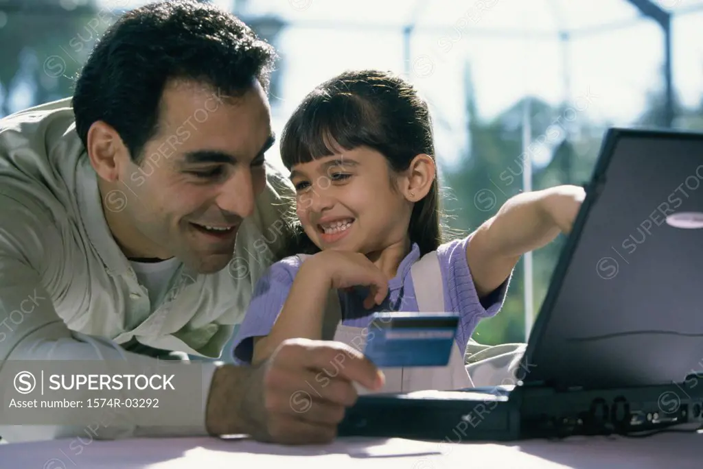 Father and his daughter in front of a laptop holding a credit card