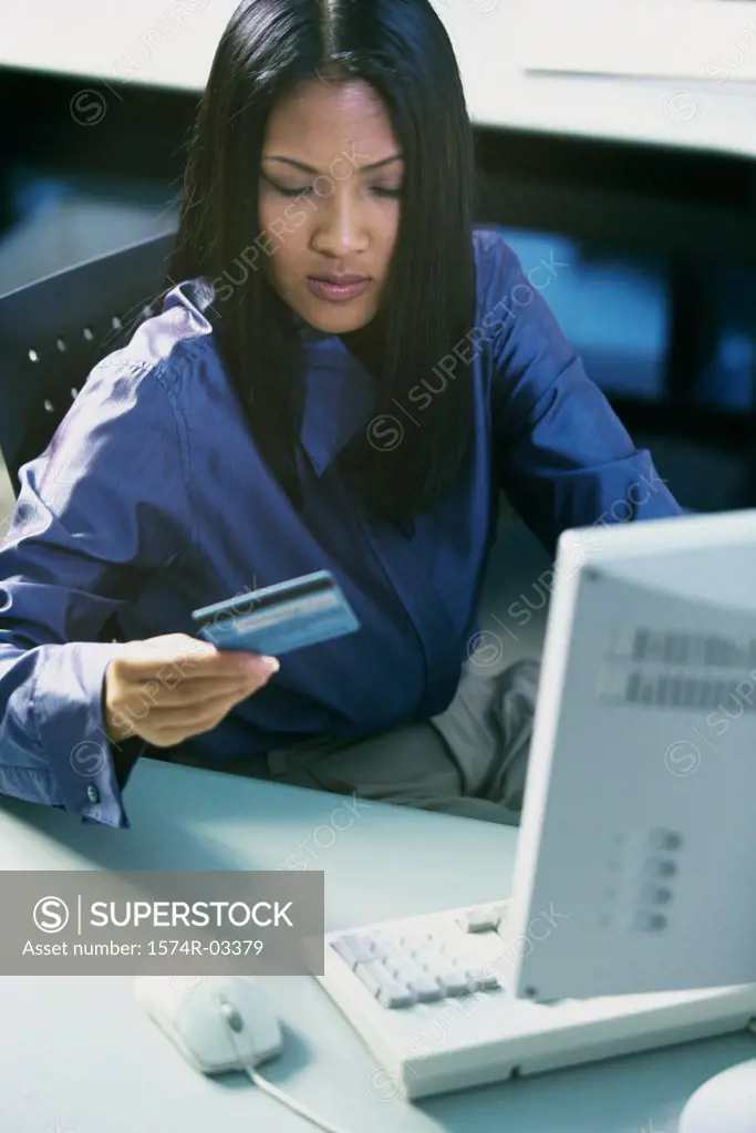 High angle view of a young woman sitting in front of a computer holding a credit card
