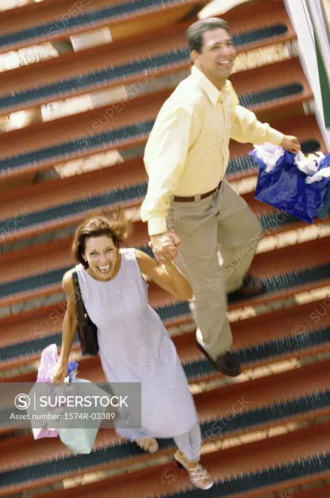 Portrait of a mid adult couple walking down stairs carrying shopping bags