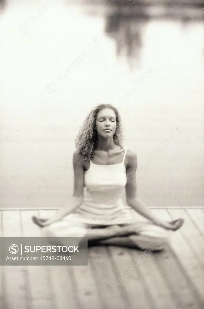 Young woman sitting on a pier meditating