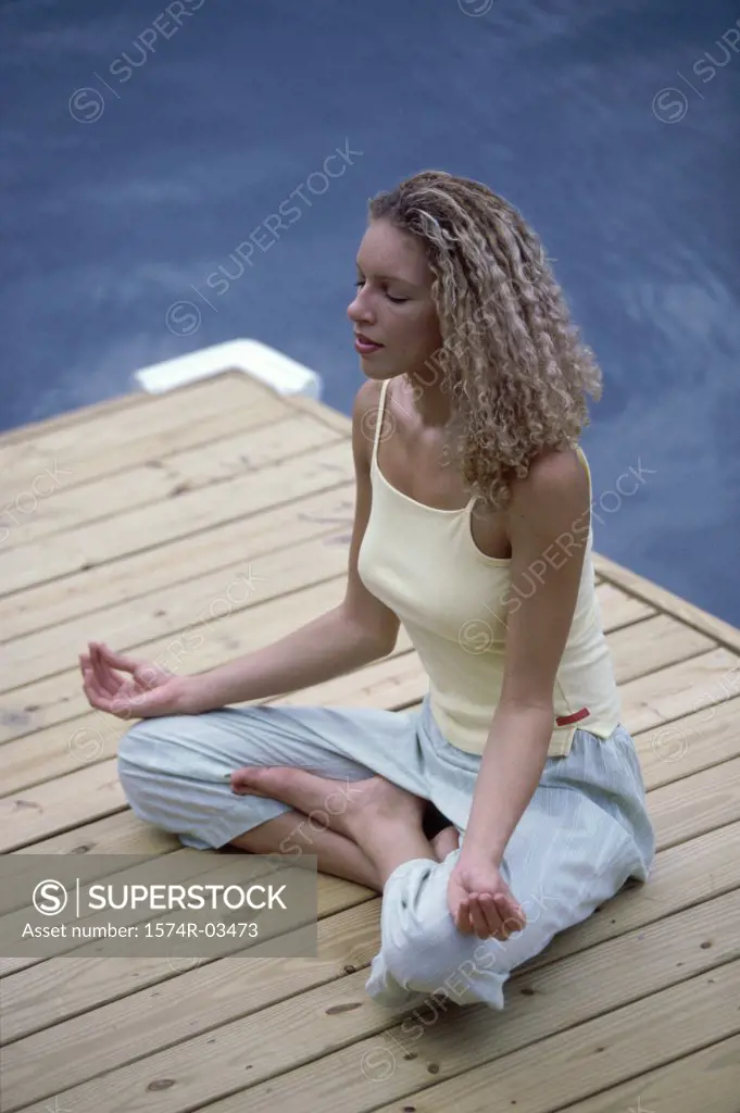 Young woman sitting on a wooden porch meditating