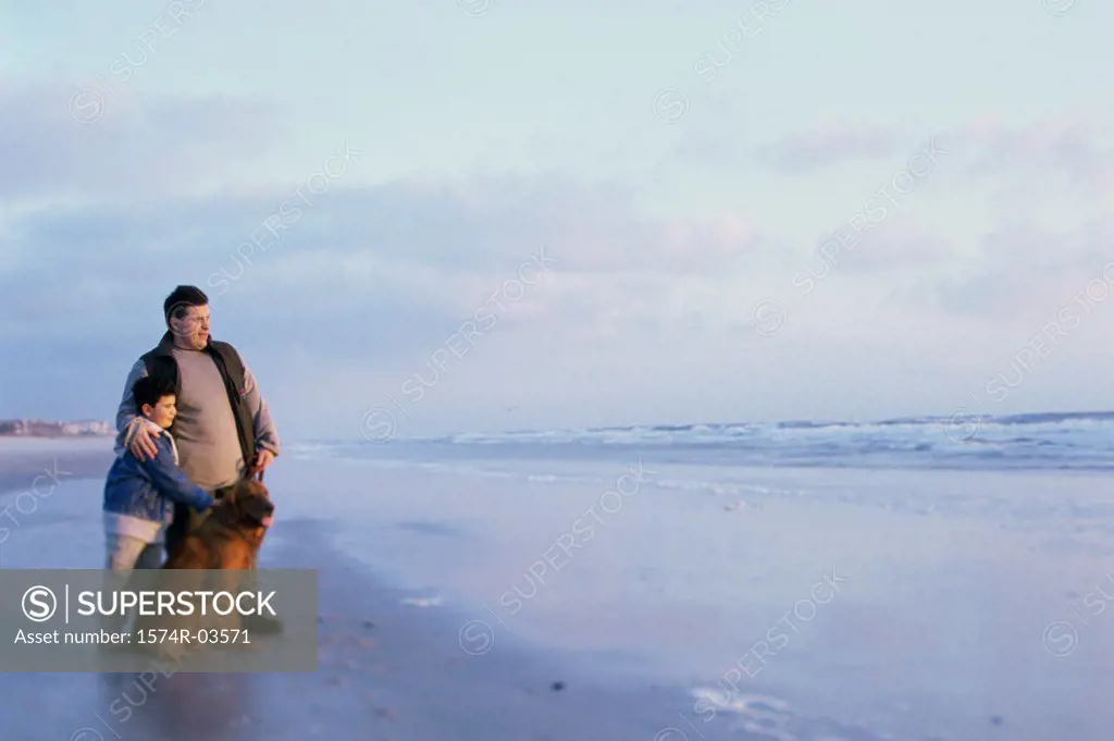 Father and his son standing with their dog on the beach