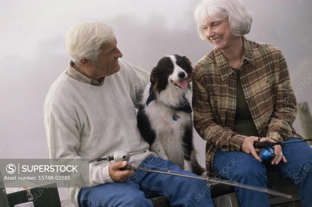 Senior couple sitting on a dock with their dog fishing