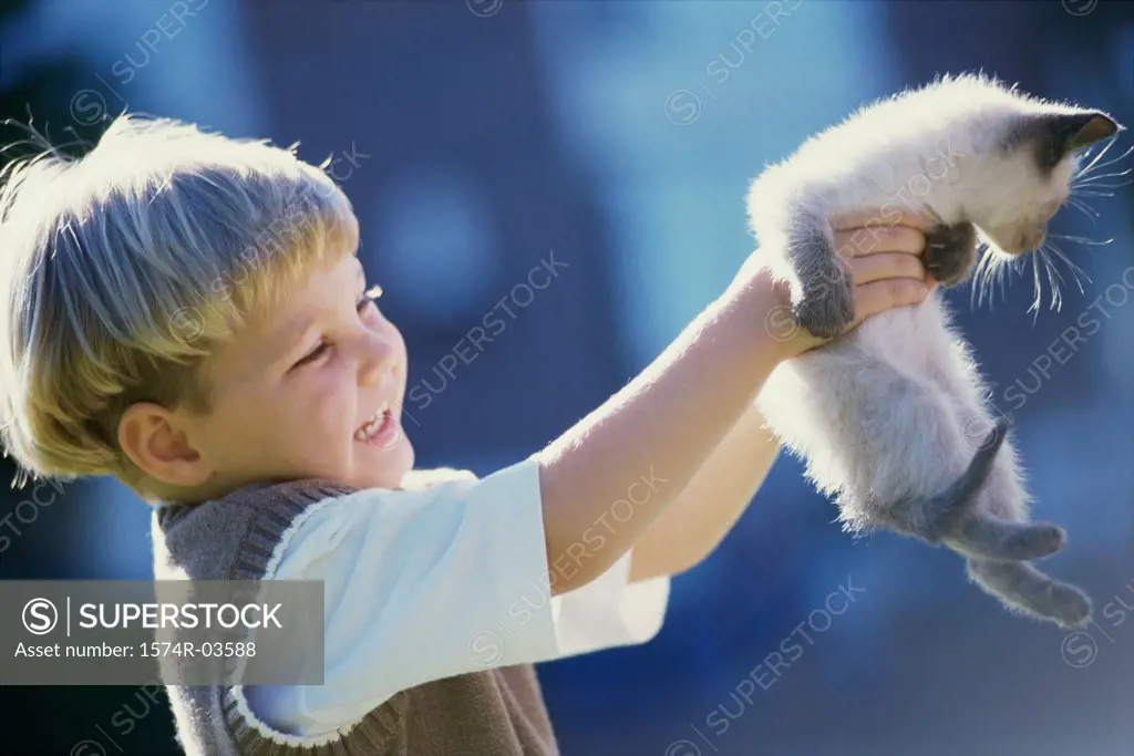 Side profile of a boy carrying a Siamese kitten