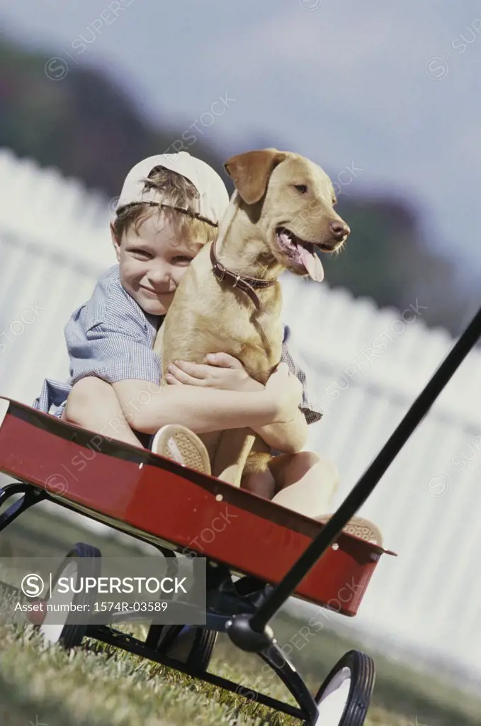 Portrait of boy sitting in a toy wagon holding his dog