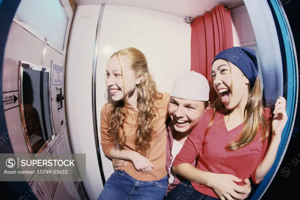 Two teenage girls and a teenage boy sitting in a photo booth