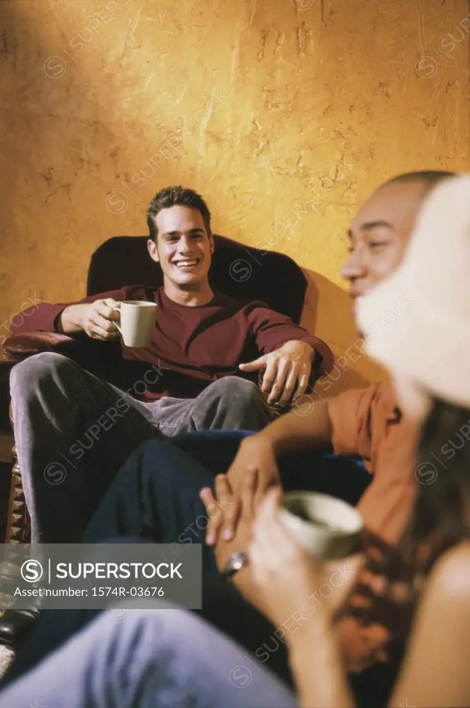Two young men and a young woman sitting in a cafe drinking coffee