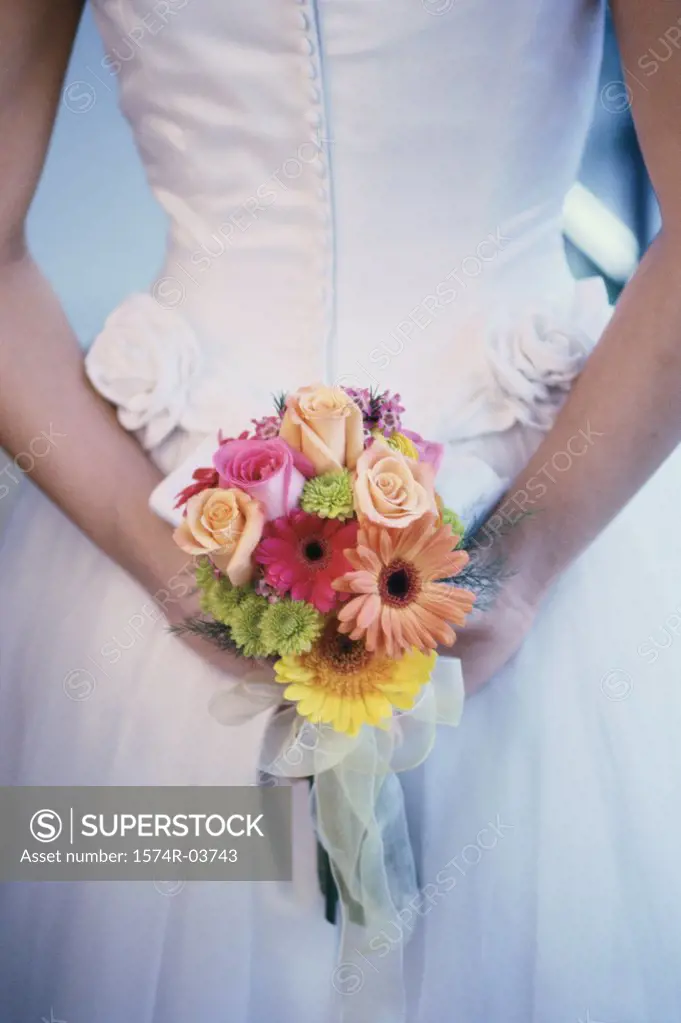 Mid section view of a bride hiding a bouquet of flowers