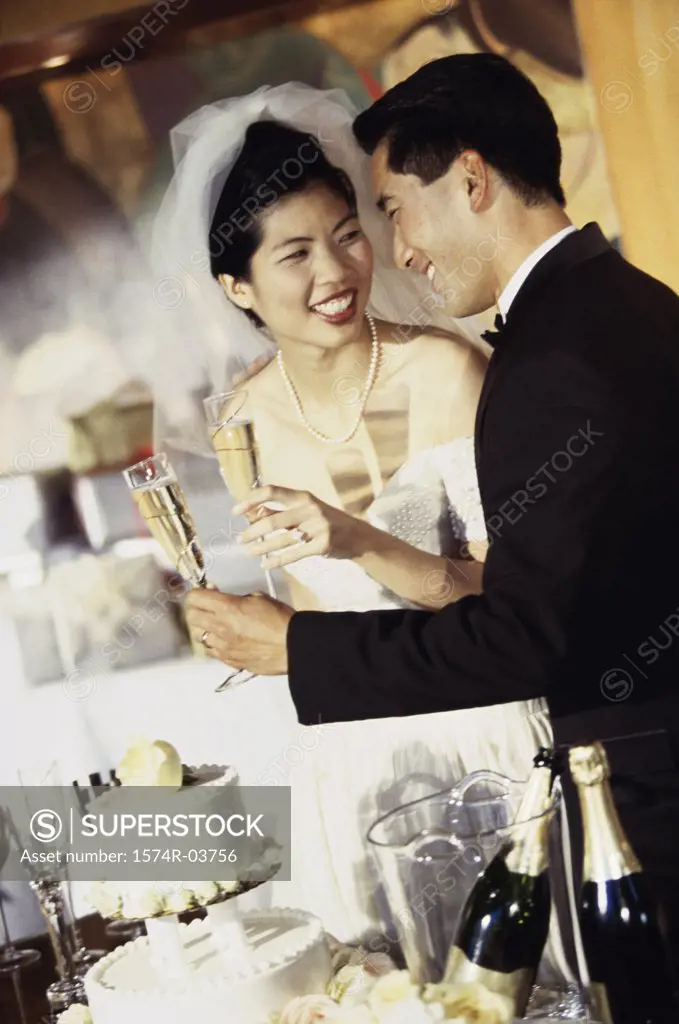 Newlywed couple standing near a wedding cake and toasting with glasses of champagne