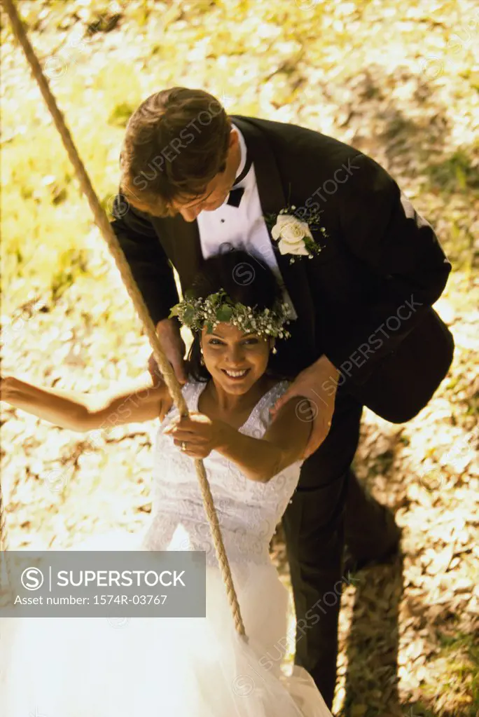 Portrait of newlywed young woman sitting on a swing with a her groom pushing her