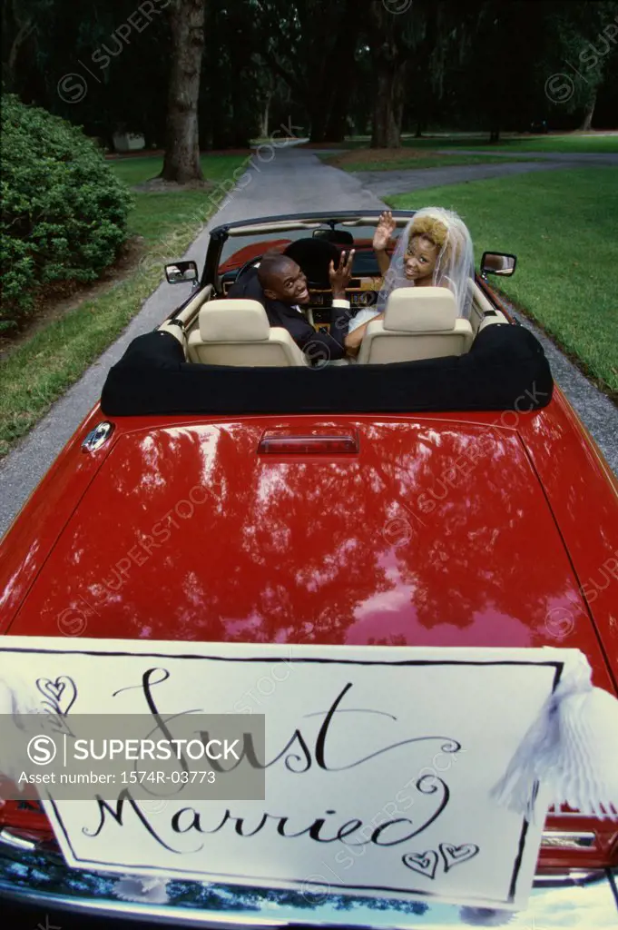 Portrait of a newlywed couple waving from a convertible car