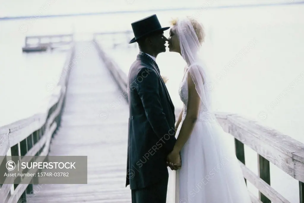 Side profile of a newlywed couple kissing on a pier