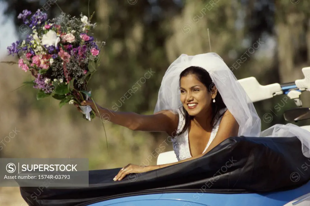 Bride preparing to toss a bouquet of flowers from a convertible car