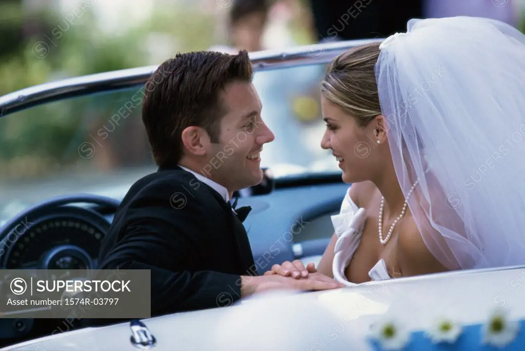 Side profile of a newlywed couple looking at each other in a convertible car