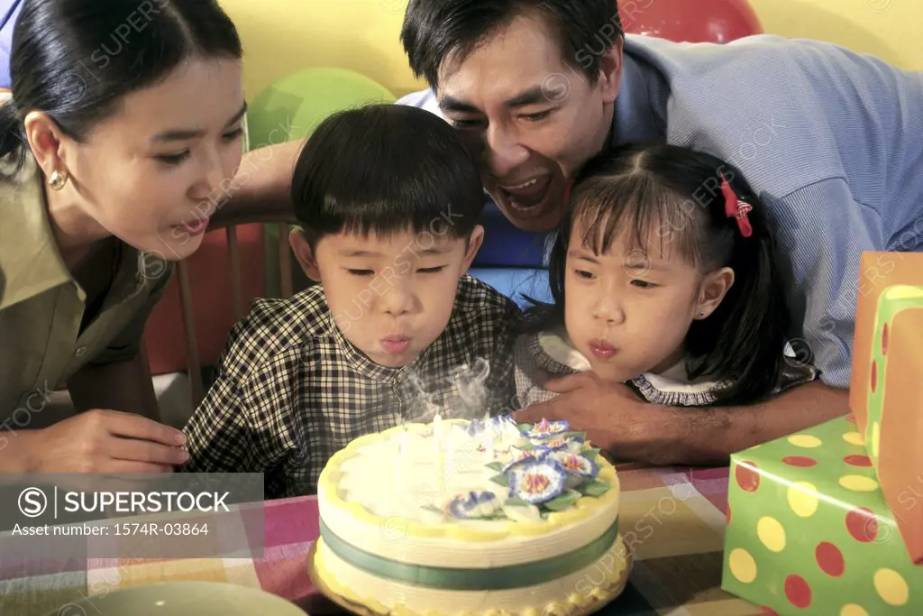 Son and daughter blowing out candles on their birthday cake with their parents behind them