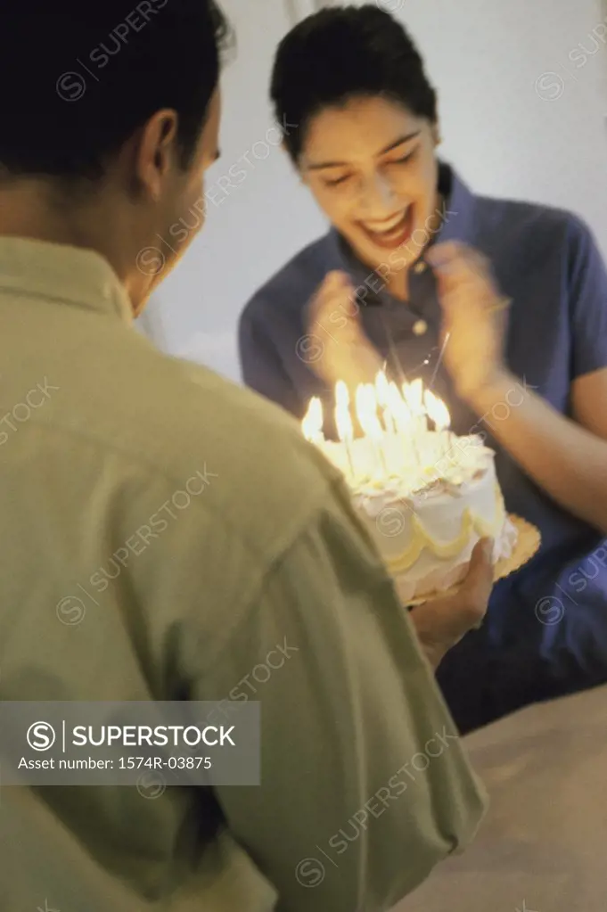 Mid adult man holding a birthday cake in front of a mid adult woman