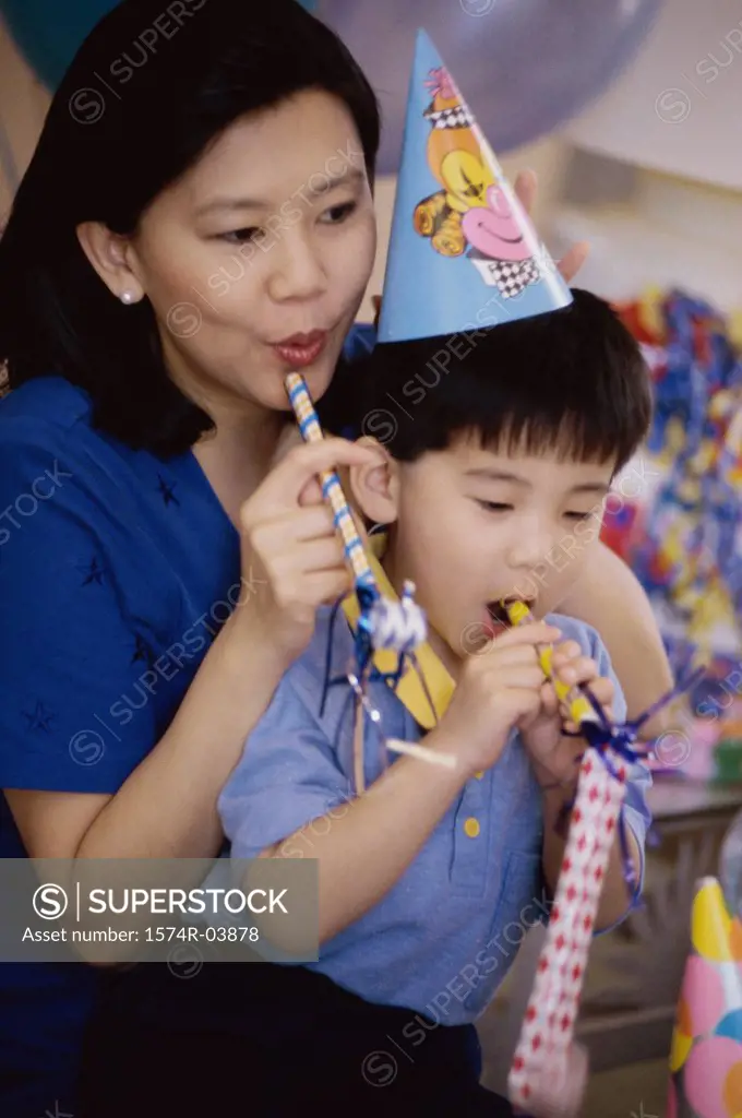 Boy wearing a birthday cap blowing a party horn blower with his mother