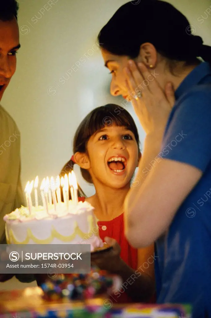 Girl standing in front of a birthday cake with her parents