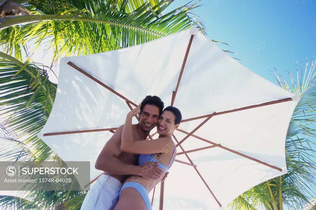 Portrait of a young couple holding each other under a beach umbrella