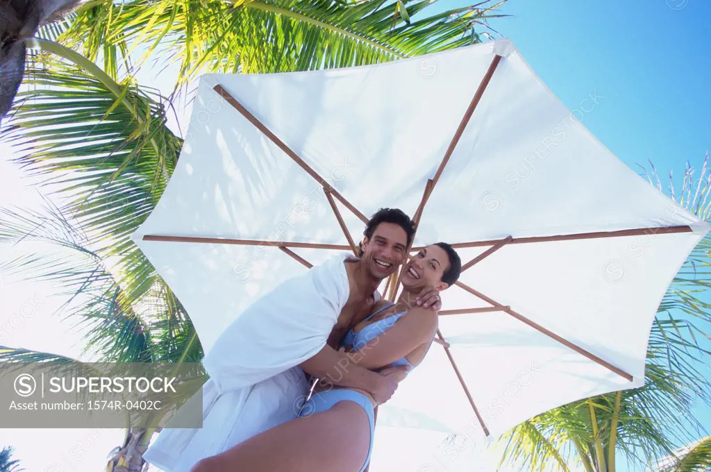Portrait of a young couple holding each other under a beach umbrella