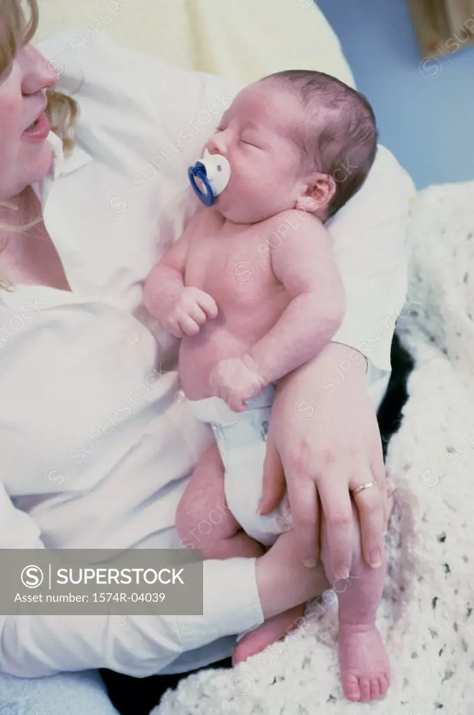 Close-up of a baby boy sucking on a pacifier sleeping in his mother's arms