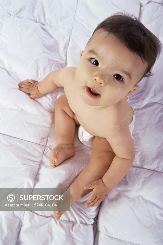 High angle view of a baby boy sitting on a bed