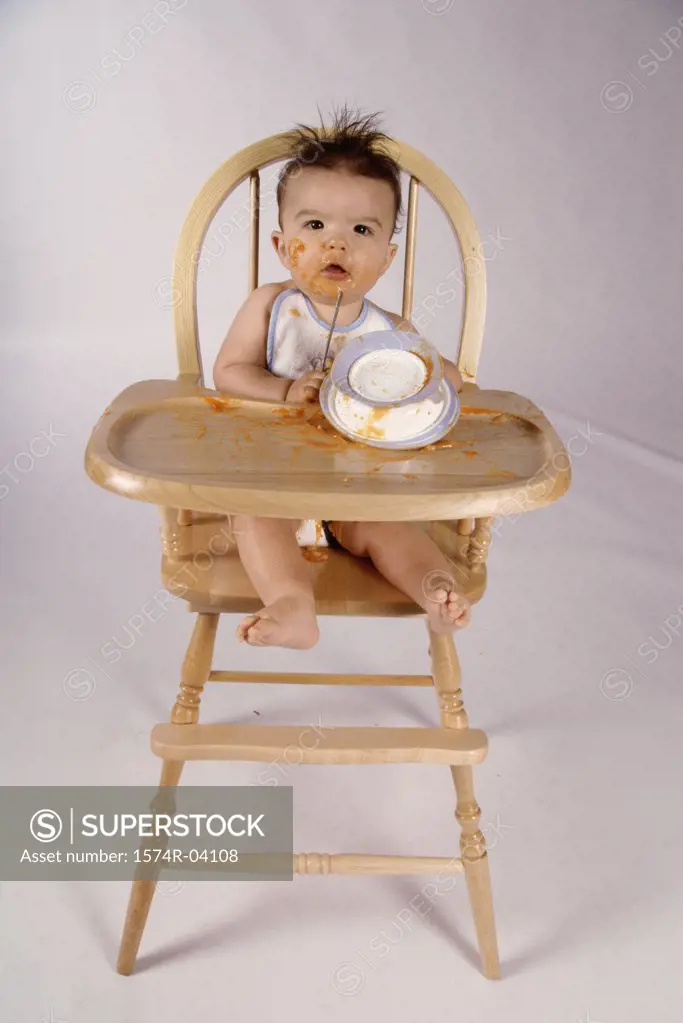 Portrait of a baby boy sitting in a high chair playing with a bowl