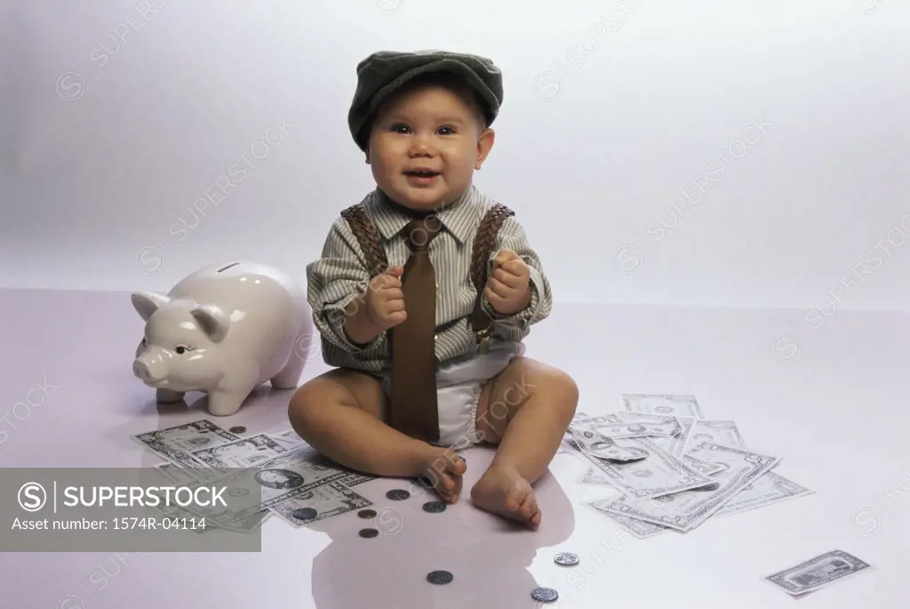 Portrait of a baby boy sitting on the floor with a piggy bank and money