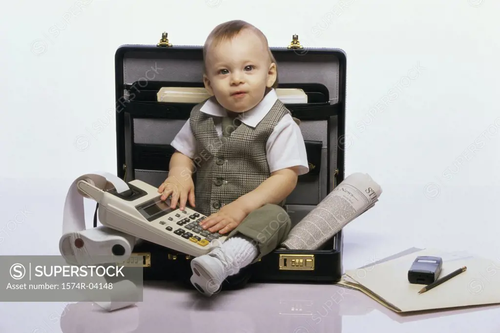 Portrait of a baby boy sitting in an open briefcase holding an adding machine