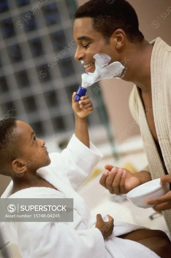 Side profile of a boy applying shaving cream on his father's face