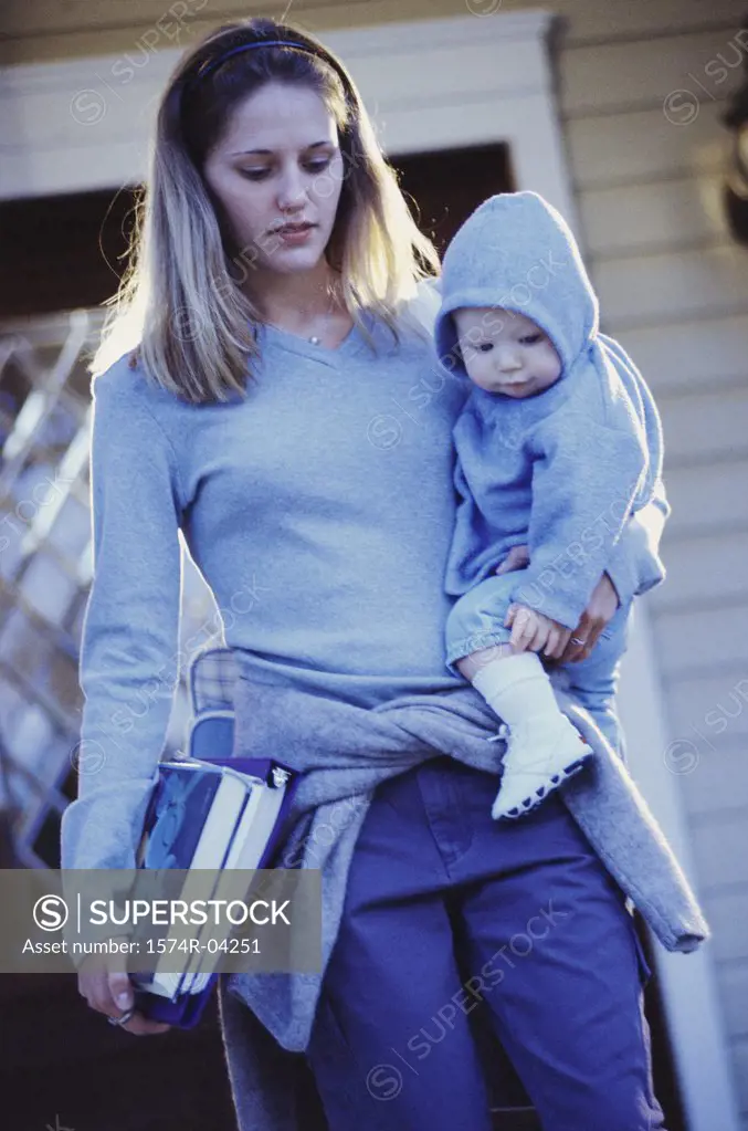 Teenage girl carrying her baby boy and books