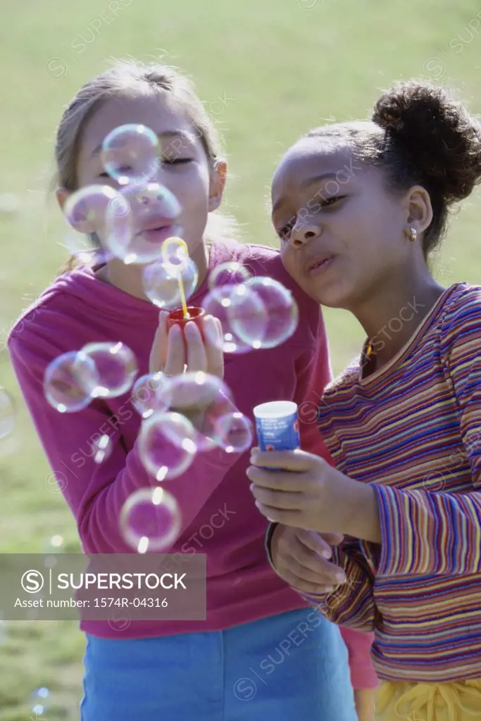 Close-up of two girls blowing bubbles with a bubble wand