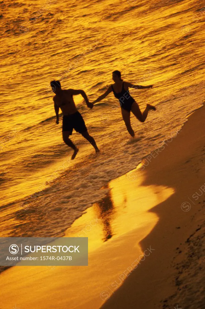 Silhouette of a young couple running at the beach holding hands