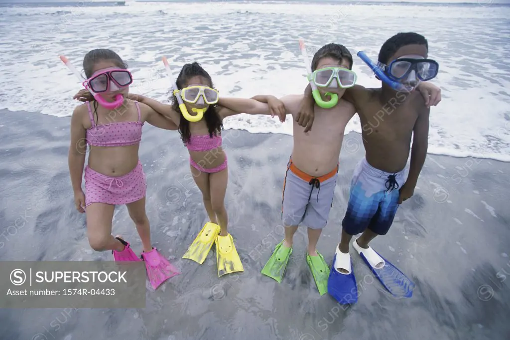 Portrait of two boys and two girls wearing snorkels standing in a row on the beach