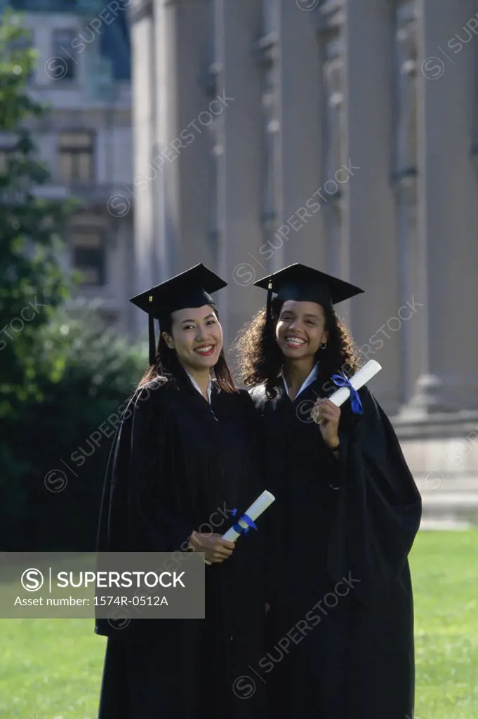 Two young women wearing graduation outfits holding diplomas